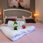 Ein Bett mit rosa Bettwäsche, weißen Kissen und einer Flasche Wein.