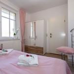 Schlafzimmer mit rosa Bettwäsche, Fenster, Kleiderschrank und Stuhl.