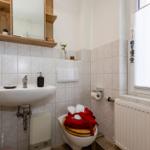 Badezimmer mit Waschbecken, Toilette und Fenster mit Jalousie.