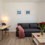 Ein Wohnzimmer mit Sofa, Tisch und Blumen. Wandbilder und Vorhänge sind sichtbar.