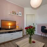 Wohnzimmer mit TV, Schreibtisch und Blumen. Wandfarbe rosa.