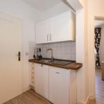 Küche mit Spüle, Herd und Kühlschrank. Tür und Blick in Wohnzimmer.