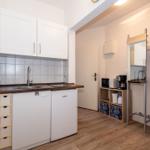 Küche mit Spüle, Kühlschrank und Kochfeld. Nebenraum mit Spiegel und Küchengeräten.