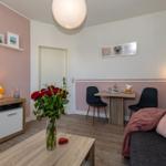 Wohnzimmer mit Sofa, Esstisch, Fernseher und Blumen.
