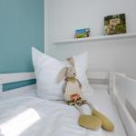 Ein Kinderbett mit Kissen, Stofftier und Büchern auf Regal.
