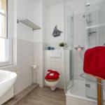 Badezimmer mit Badewanne, Dusche und Toilette. Rote Handtücher und Segelschiff-Dekoration.