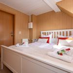 Schlafzimmer mit Holzwänden, weißem Bett und roten Kissen.