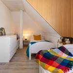 Zwei Betten unter Dachschrägen mit Holzwand und Schrank.