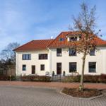 Zweistöckiges Haus mit rotem Dach und Vorgarten. Eingangstür und Fenster sind sichtbar.