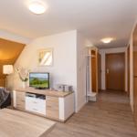 Wohnzimmer mit Sofa, Fernseher und Schlafzimmer im Hintergrund.