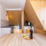 Küche mit Essbereich unter Holzdecke. Tisch mit Wein und Apfel. Fenster mit Tulpen.