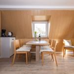 Essbereich mit Holztisch, Stühlen und Fenster. Küche mit Kaffeemaschine und Kühlschrank.