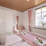 Schlafzimmer mit Bett, Kleiderschrank und Fenster mit rosa Vorhängen.