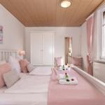 Schlafzimmer mit Doppelbett, rosa Decke, Fenster und Schrank.