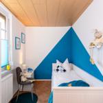 Kinderzimmer mit Bett, Stuhl und Fenster. Wand in Blau und Weiß.
