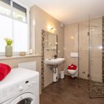 Badezimmer mit Dusche, Waschbecken und Waschmaschine. Fenster mit Blumen.
