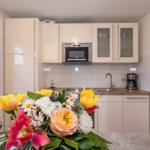 Küche mit weißen Schränken, Spüle und Mikrowelle. Blumenarrangement im Vordergrund.