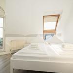 Schlafzimmer mit Dachschräge, großem Fenster und weißem Bett.