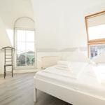 Schlafzimmer mit Doppelbett, zwei Fenstern und Holzboden.