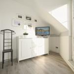 Schlafzimmer mit TV, Kleiderständer und großem Fenster.