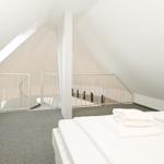 Schlafzimmer mit Dachschrägen, weißem Bett und Dachfenster. Geländer führt zur Treppe.