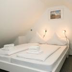 Schlafzimmer mit Doppelbett, weißen Laken und zwei Wandlampen.