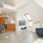 Wohnbereich mit TV, blauer Sessel und Küchenbereich im Hintergrund.