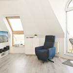 Wohnraum mit blauem Sessel, TV und Balkonansicht.