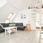 Wohnzimmer mit grauem Sofa, weißem Tisch und Wendeltreppe.