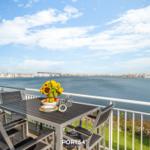 Terrasse mit Tisch und Stühlen, Blick auf Wasser und Hafen.