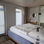 Schlafzimmer mit Bett, Kleiderschrank und Fenstern.