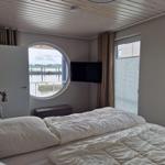 Schlafzimmer mit Rundfenster zum Wasser und Fernseher an der Wand.