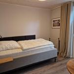 Schlafzimmer mit Bett, Nachttisch und Fenster mit Vorhängen.