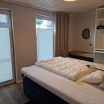 Schlafzimmer mit Doppelbett, Kleiderschrank und Fenstern mit Jalousien.