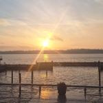 Sonnenuntergang über dem Wasser mit Steg und Gebäude im Vordergrund.