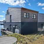 Modernes Haus am Wasser mit Holz- und Metallfassade, Bootssteg und Terrasse.