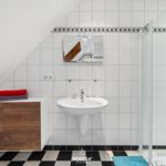 Badezimmer mit Dusche, Waschbecken und Holzschrank unter Dachschrägen