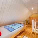 Schlafzimmer mit Holzboden und Dachschrägen. Bett mit blauer Bettwäsche und rotem Kissen.