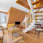 Wohnbereich mit Treppe, Sitzmöbeln und TV. Holzdecke und Boden.