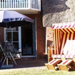 Terrasse mit Sonnenschirm, Stühlen und Strandkorb vor einem Haus mit Dach aus Stroh.