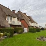 Reihenhaus mit Strohdach und weißen Balkonen vor grünem Rasen.