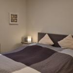 Schlafzimmer mit Bett, Nachttisch und Fenster mit Jalousie.