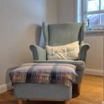 Ein grauer Sessel mit Kissen und Fußhocker auf Holzboden.