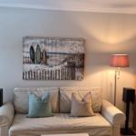 Wohnzimmer mit Sofa, Schreibtisch und Wandbild mit Surfbrettern.