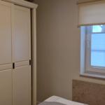 Schlafzimmer mit Kleiderschrank und Fenster mit Rollladen.