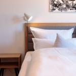 Schlafzimmer mit Bett, Nachttisch und Wandlampe. Wandbild über dem Kopfteil.