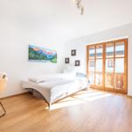 Schlafzimmer mit Bett, Holzboden und Glas-Tür zur Terrasse.