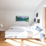 Schlafzimmer mit Bett, Tisch und Wandbild. Holzfenster und helles Holzfußboden.