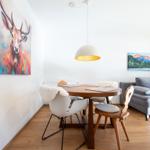Esszimmer mit Tisch, Stühlen und Wandbildern. Sofa im Hintergrund.