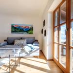 Wohnzimmer mit Sofa, Tischen und großem Fenster. Wandbild zeigt Berge.